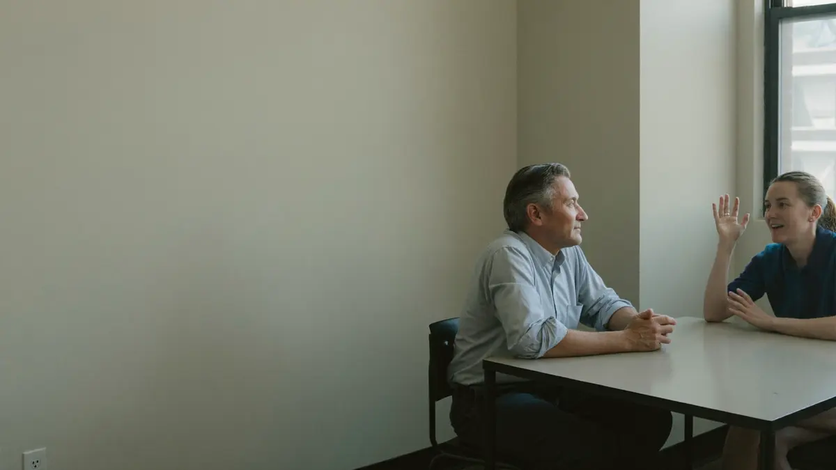 Two colleagues in a brokerage office talking across a meeting table